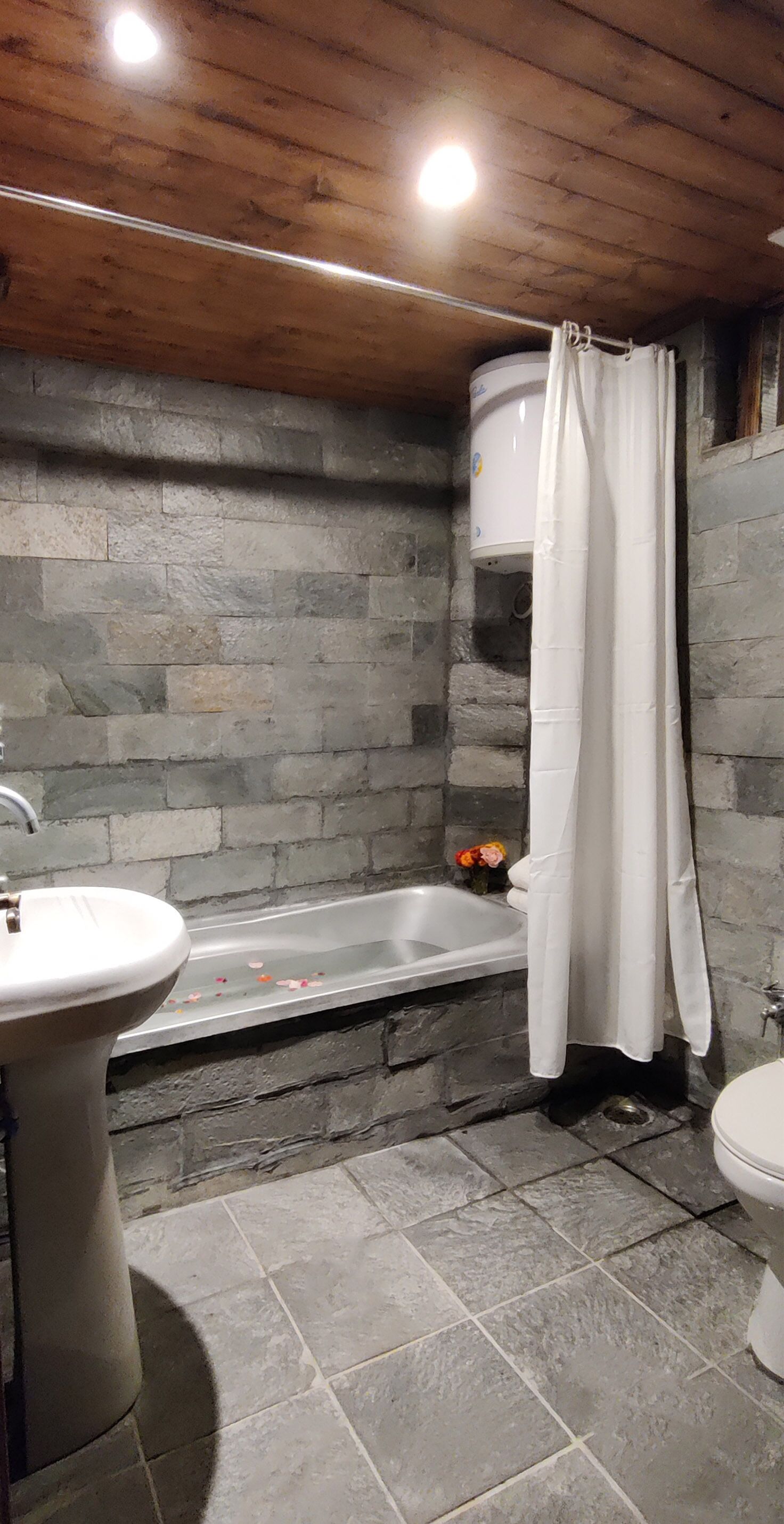Un baño con pared de piedra, una bañera, un lavamanos y un inodoro.