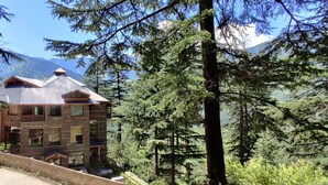 Un bâtiment en pierre, doté d’un toit en pente, entouré d’une forêt dense et de montagnes.