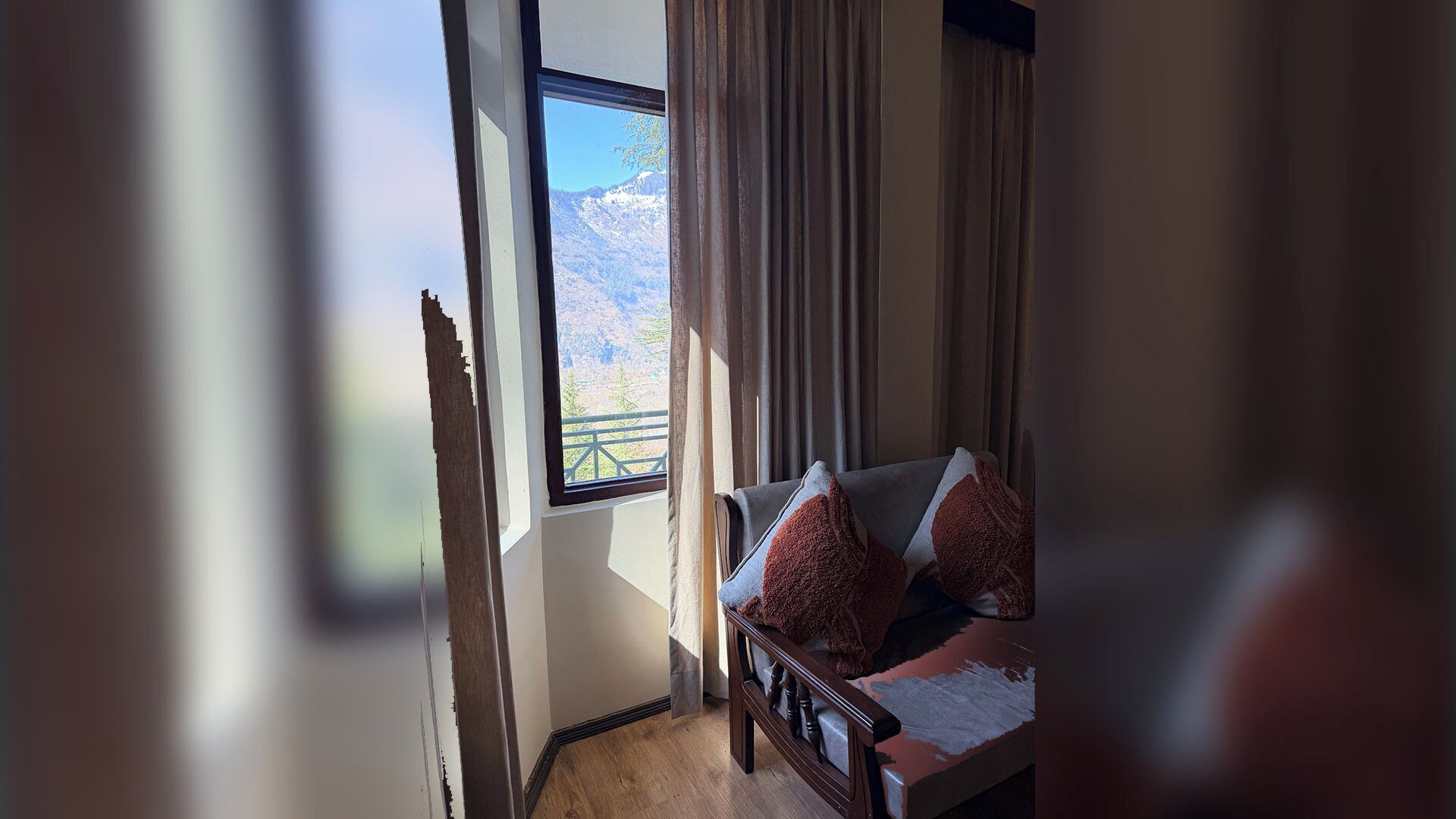 Una habitación con vistas a las montañas a través de una ventana, un sofá con cojines y cortinas.