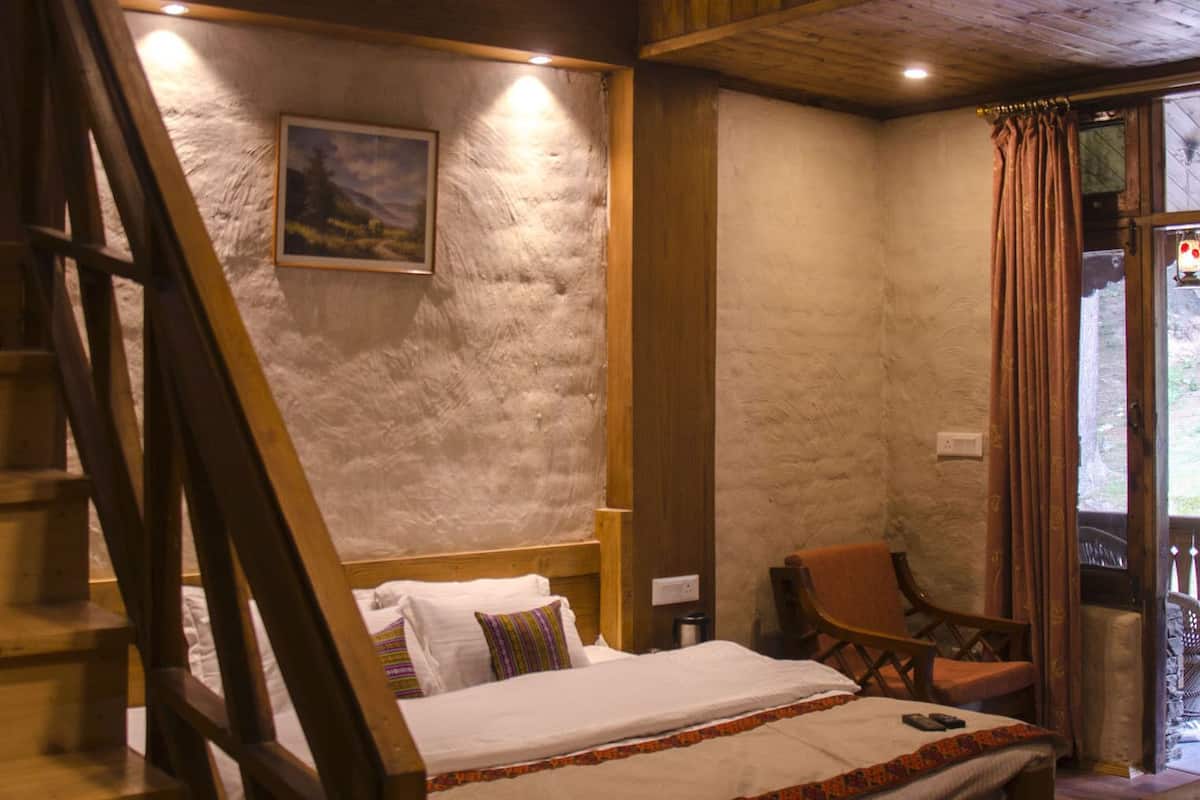Une chambre avec un escalier en bois, un lit recouvert d’une couvre-lit à motifs, une chaise et un tableau accroché au mur.