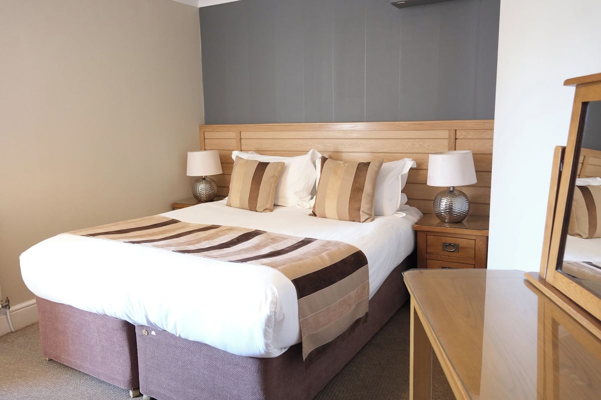 A neatly made bed with striped bedding, two bedside lamps, a wooden nightstand, and a mirror.