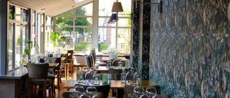 A restaurant with multiple tables and chairs, large windows, and a view of the outdoors.