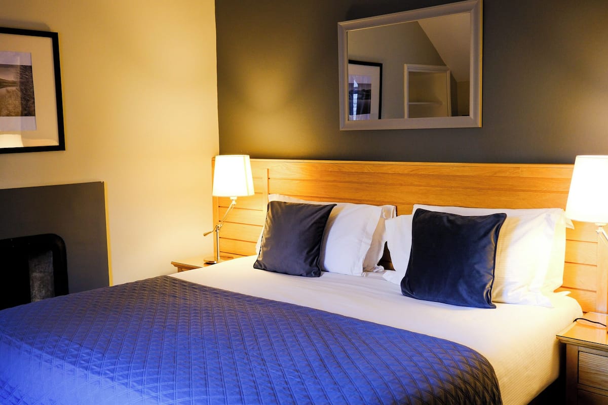 A neatly made bed with a blue quilt, two bedside lamps, and a mirror above the headboard.
