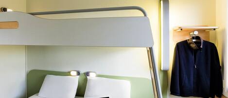 Una cama litera con una computadora portátil en la cama inferior, almohadas blancas y una prenda colgada en un estante.