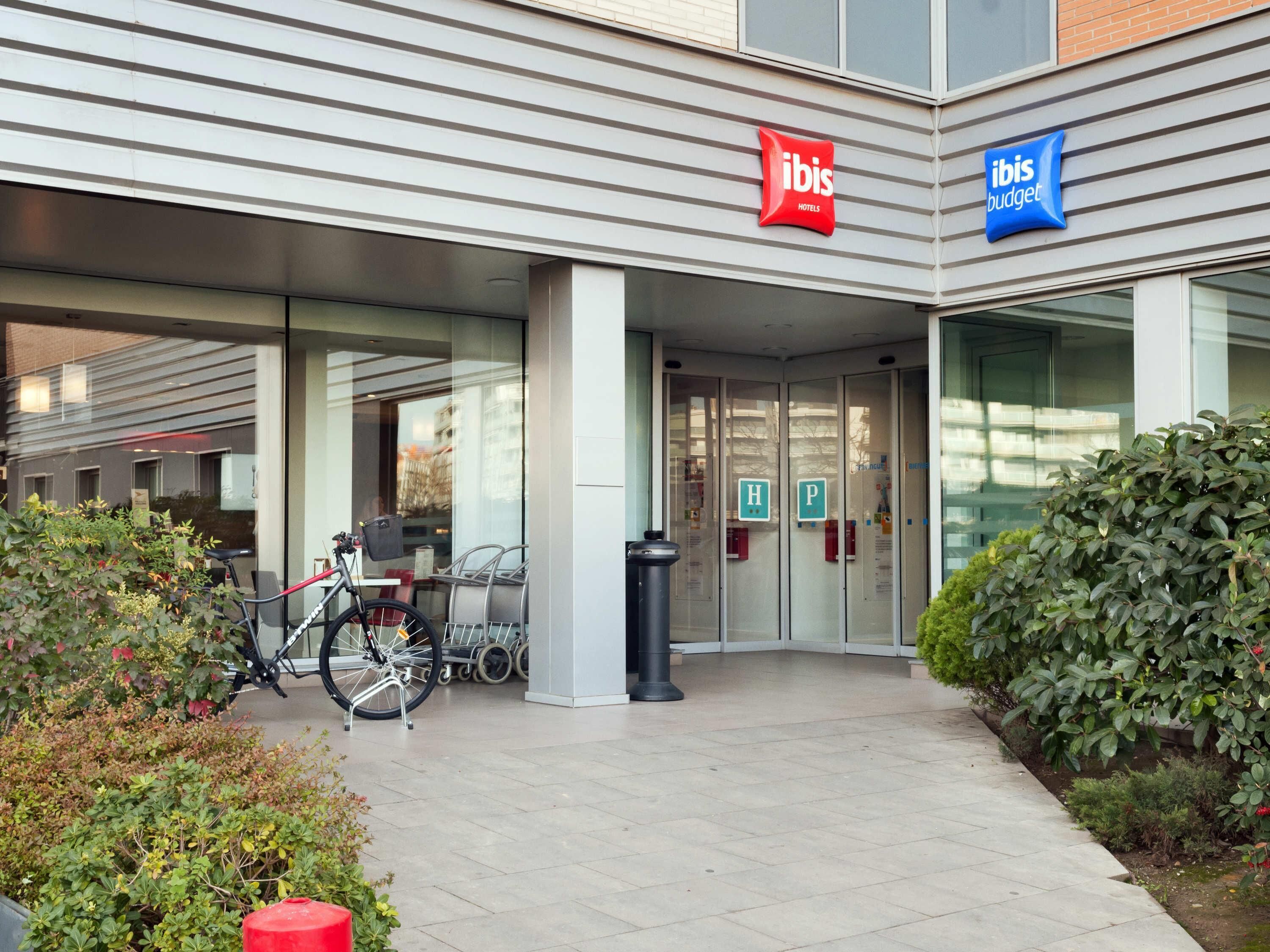 A hotel entrance with a bicycle parked outside, glass doors, and a sign for 'ibis Hotels' and 'ibis Budget'.