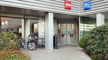 A hotel entrance with a bicycle parked outside, glass doors, and a sign for 'ibis Hotels' and 'ibis Budget'.