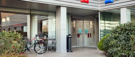Entrada de un hotel con una bicicleta estacionada afuera, puertas de vidrio y un letrero que dice 'ibis Hotels' y 'ibis Budget'.
