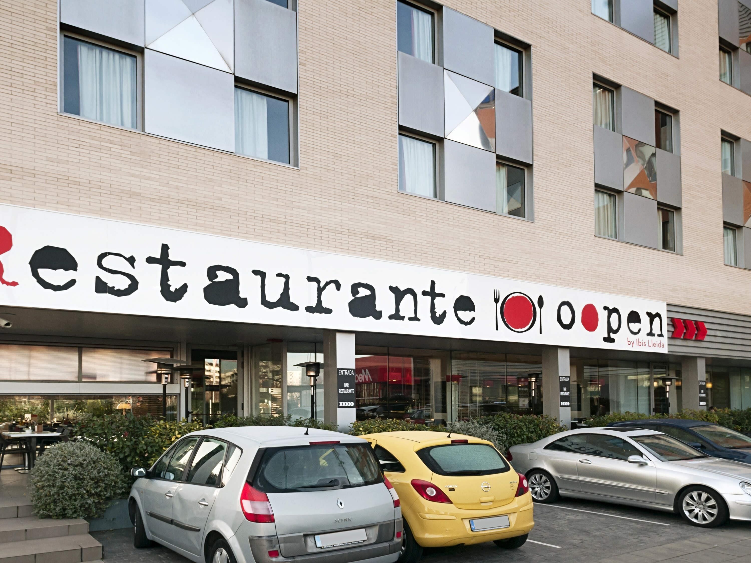 A building with a sign that reads 'Restaurante Open' and a car parked in front.
