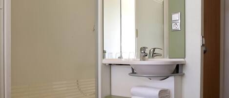 Un baño con ducha, lavamanos, espejo y toallero.