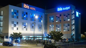 A modern hotel with a prominent "ibis HOTEL" sign, a separate "ibis budget" section, and a parking area with several cars. - ibis Lleida (Lleida)