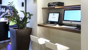 A reception area with a desk, two computer monitors, a printer, a plant, and a framed picture on the wall. - ibis Lleida (Lleida)