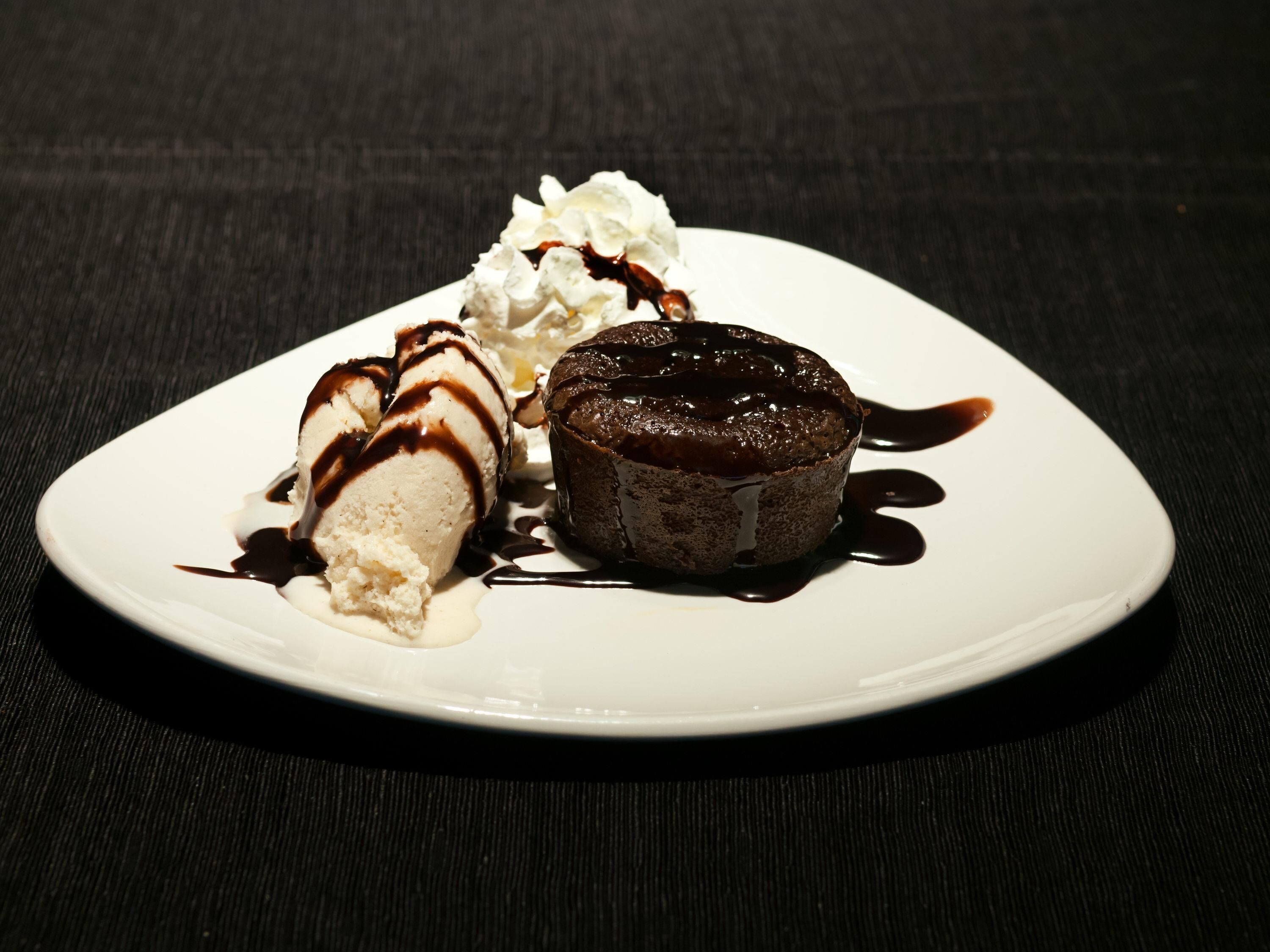 Un plato de postre con pastel volcán de chocolate, helado de vainilla y crema batida.