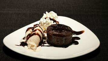 Un plato de postre con pastel volcán de chocolate, helado de vainilla y crema batida.
