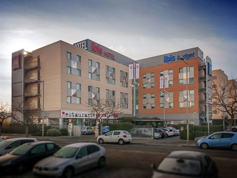 A hotel with a modern design, featuring multiple floors and a prominent 'ibis Hotel' sign. There is a restaurant named 'Restaurante Japonés' on the ground floor.