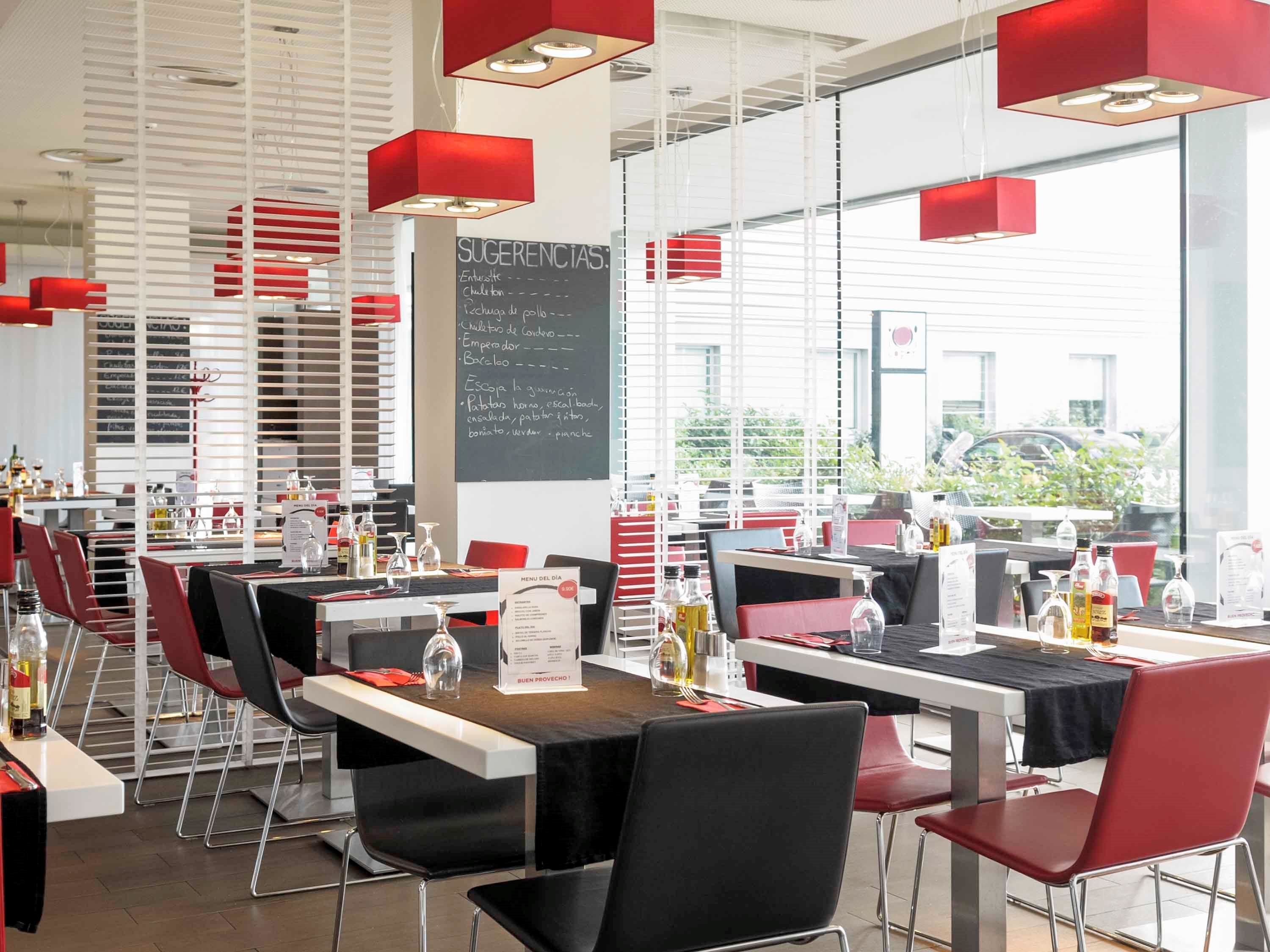 A restaurant with tables set for dining, a chalkboard menu, and red pendant lights.