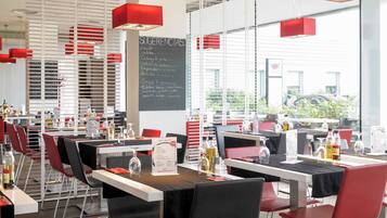 A restaurant with tables set for dining, a chalkboard menu, and red pendant lights.