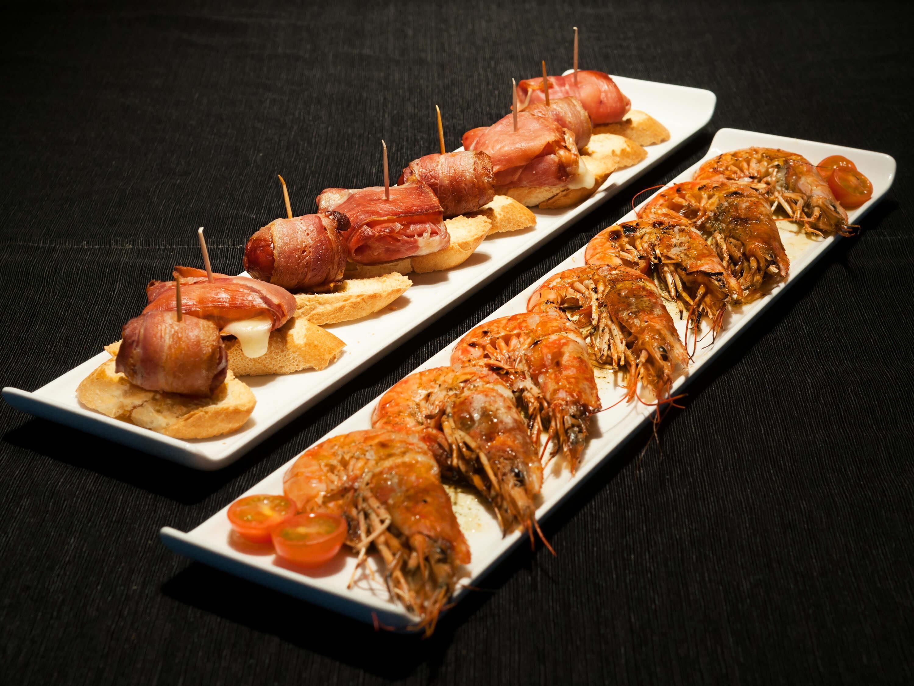 A tray of food with bacon-wrapped items and grilled shrimp, served on a white plate.