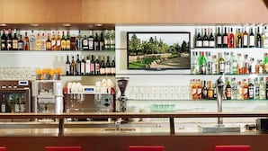 A bar area with a variety of liquor bottles, a coffee machine, and a television screen displaying a landscape. - ibis Lleida (Lleida)