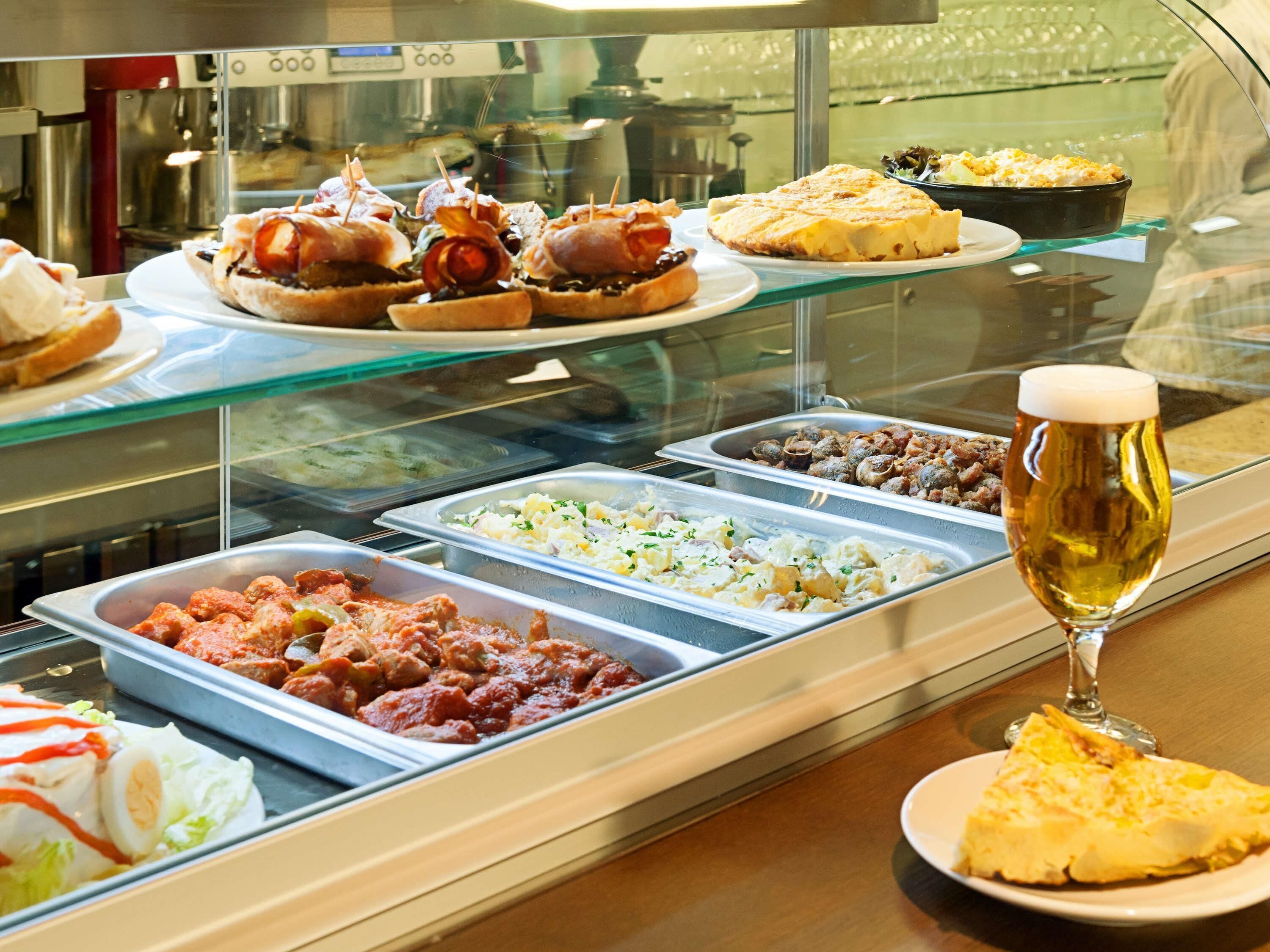 Un bufé con diversos platos, una cerveza y una porción de pizza.