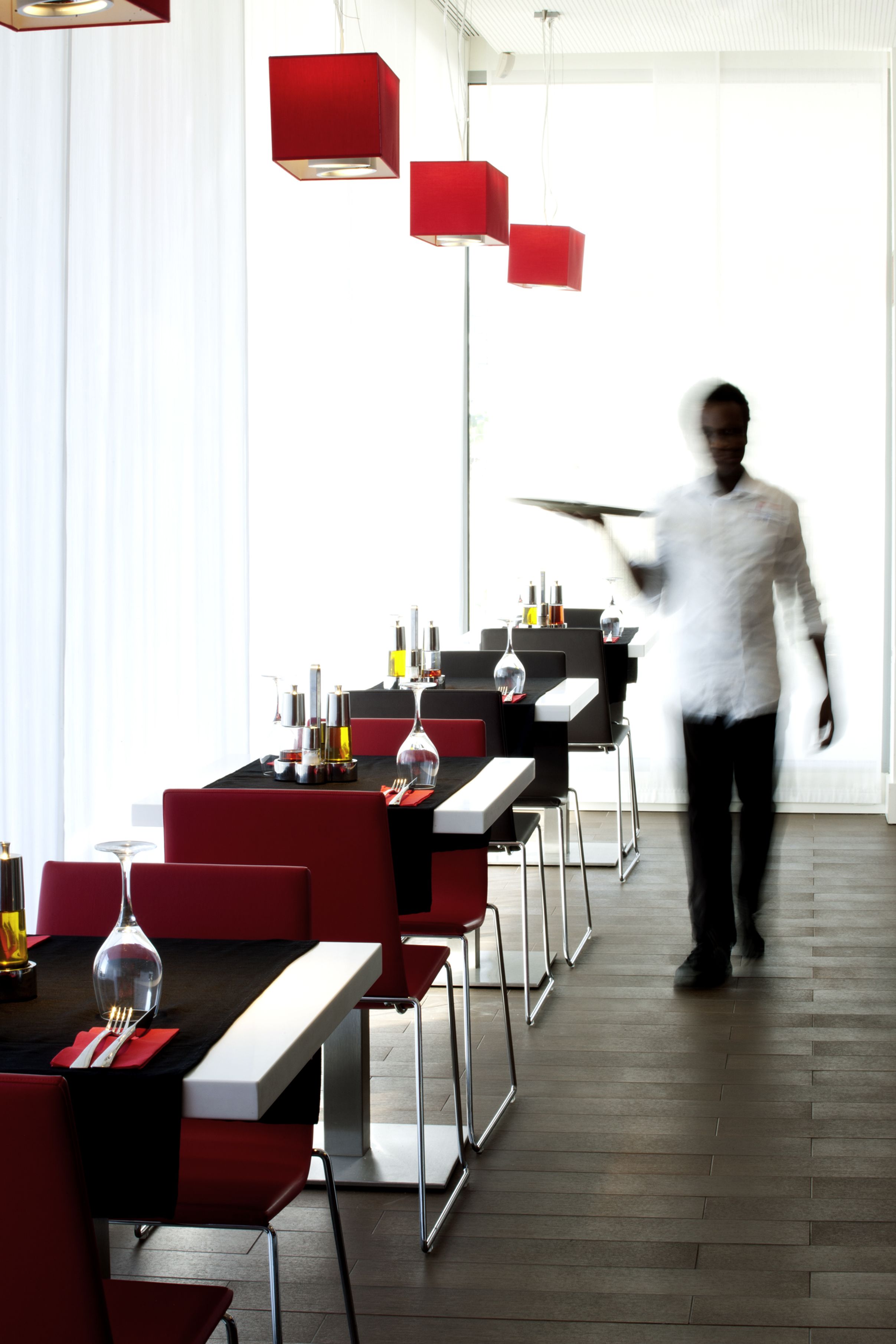 Un comedor moderno con sillas rojas, mesas negras y lámparas colgantes rojas.