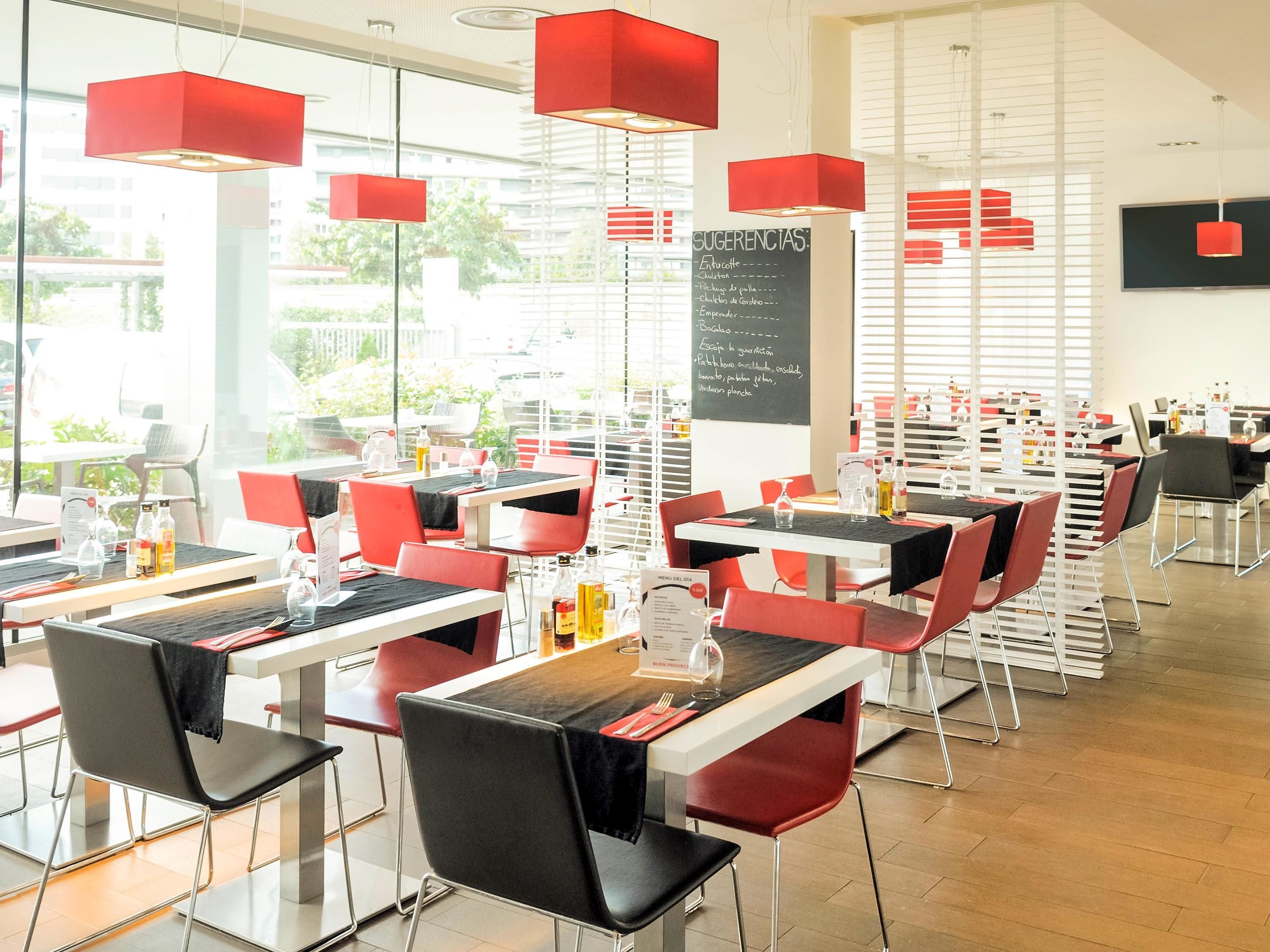 En moderne restaurant med røde og sorte stole, hvide borde samt røde hængelamper.