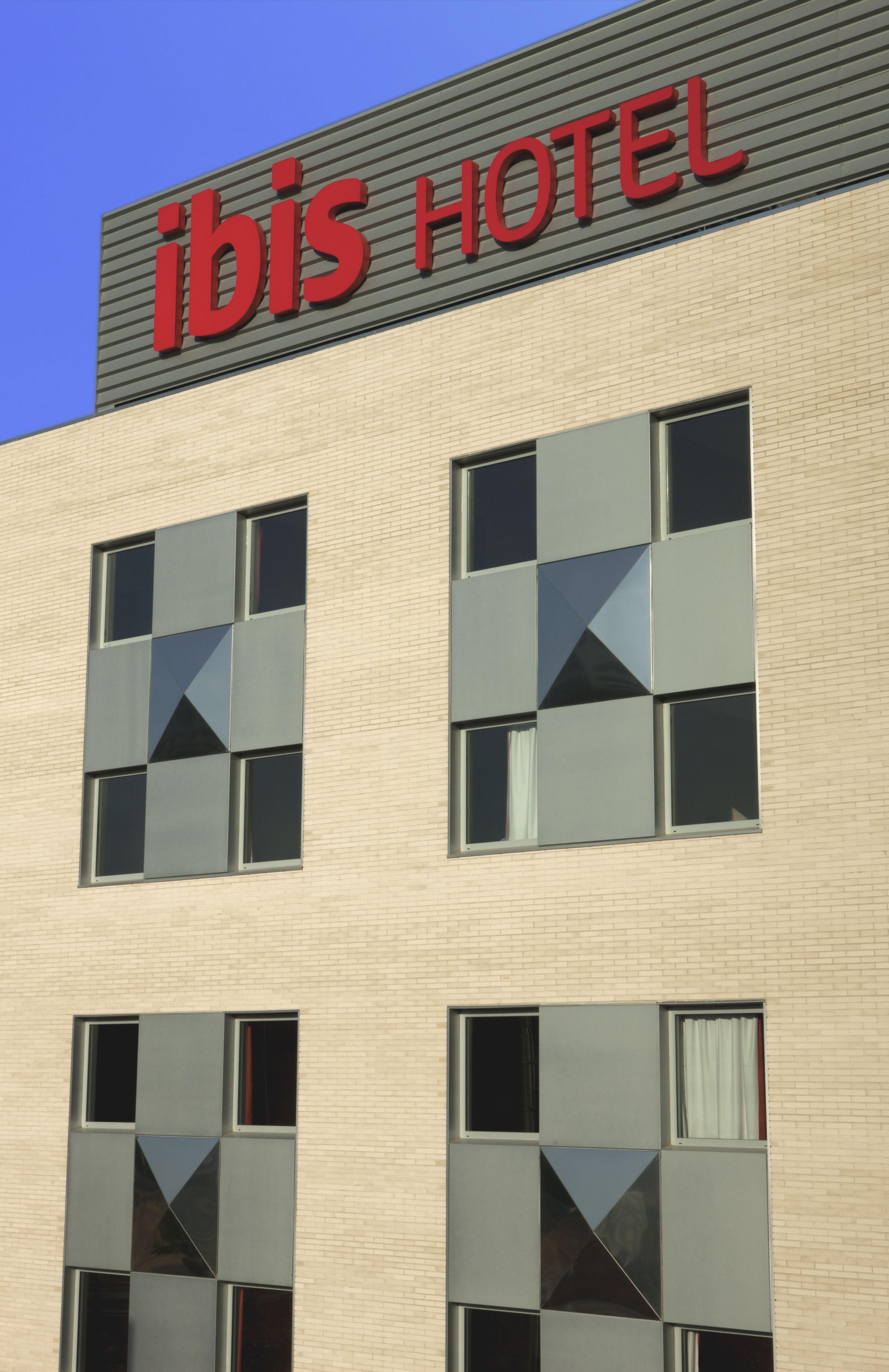 Un edificio de hotel con un letrero que dice "ibis HOTEL" y una fachada con un diseño de ventanas geométricas.