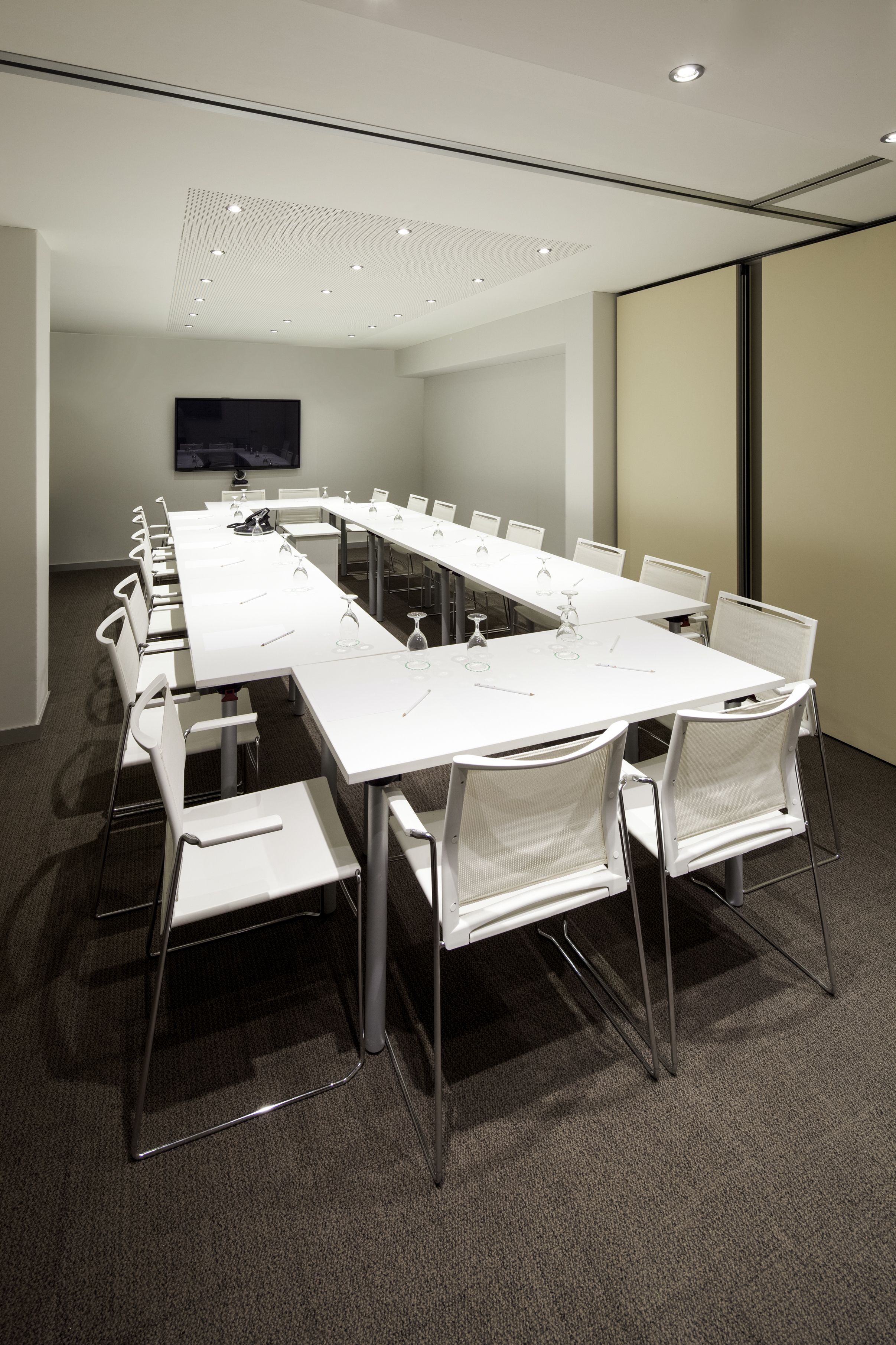 Un salón de conferencias con una mesa larga, sillas blancas y una televisión de pantalla plana en la pared.