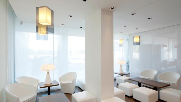 A modern hotel lobby with white furniture, large windows, and recessed lighting. - ibis Lleida (Lleida)