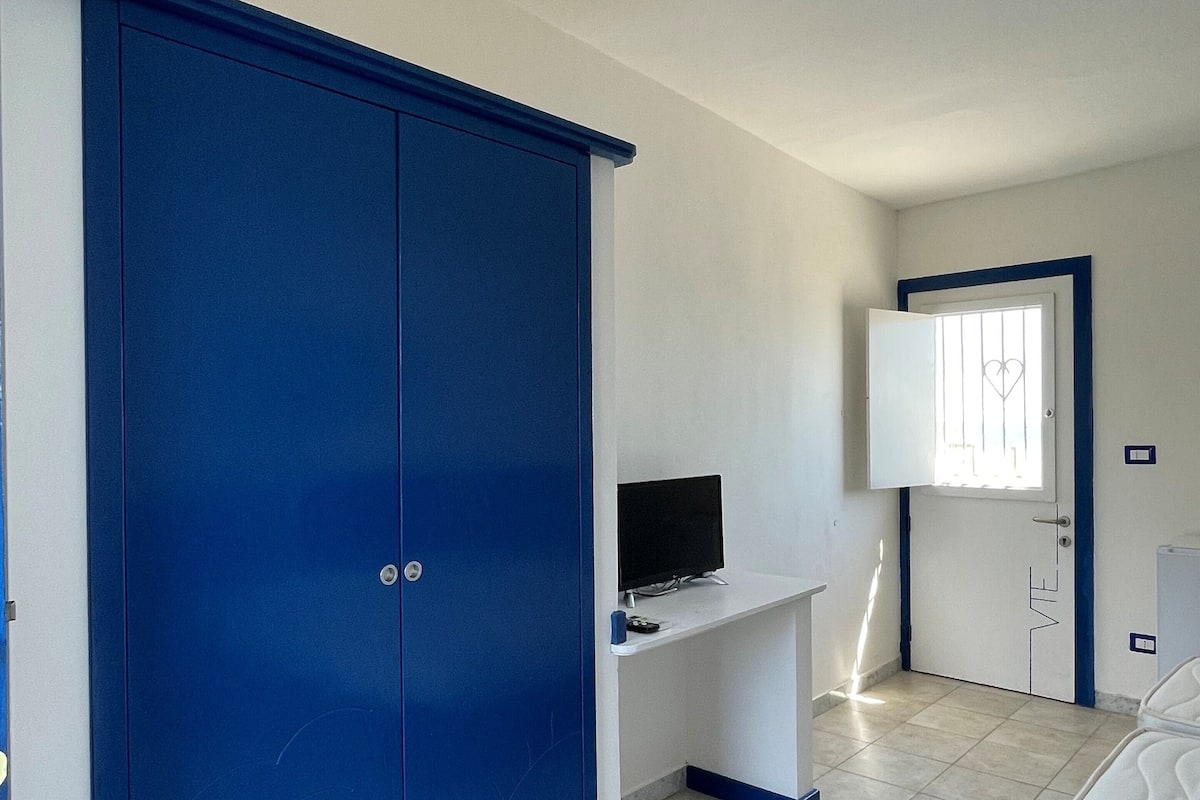 A room with a large blue wardrobe, a white desk with a computer, and a bed.