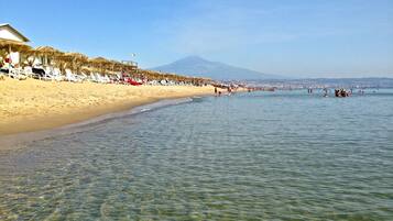 Ein Strand mit klarem, seichten Wasser, einem Sandufer und einem Berg im Hintergrund.