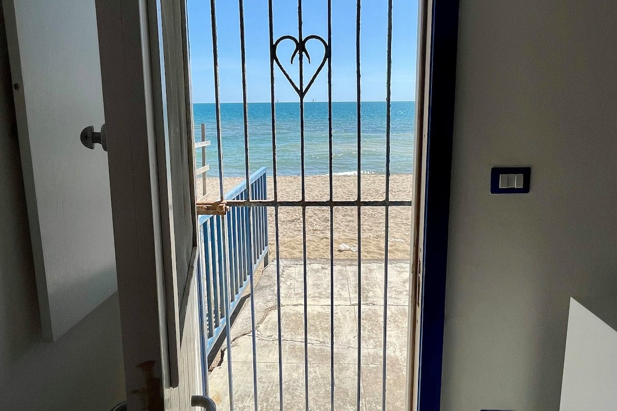 A door with a heart-shaped metal gate leading to a beach.