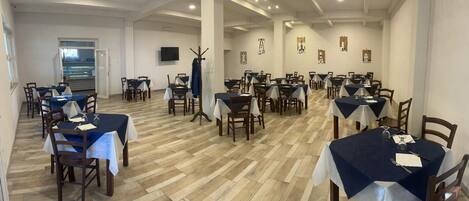 A dining area with multiple tables and chairs, a wooden floor, and a television mounted on the wall.