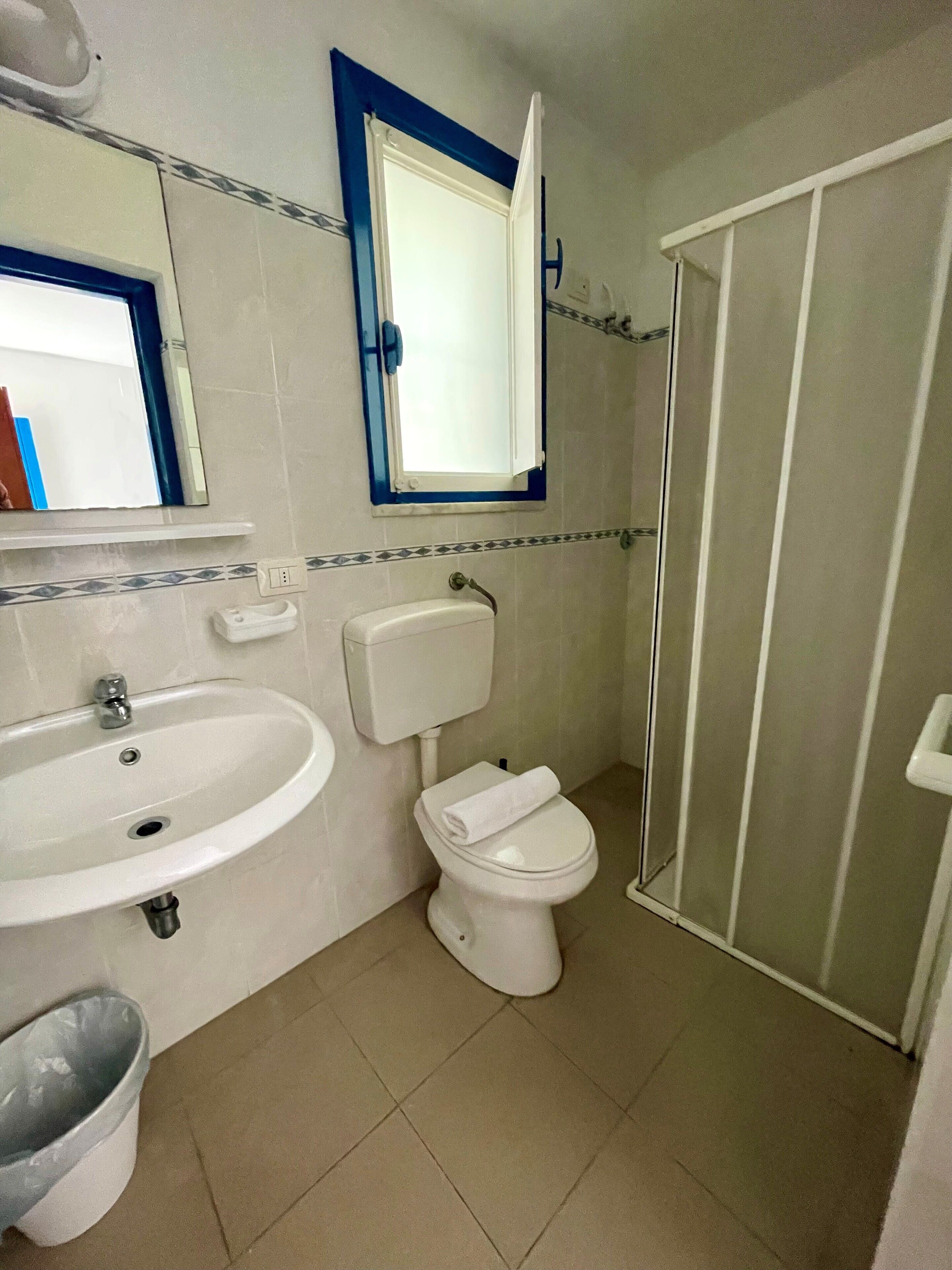 A bathroom with a sink, toilet, and a mirror with a window above it.