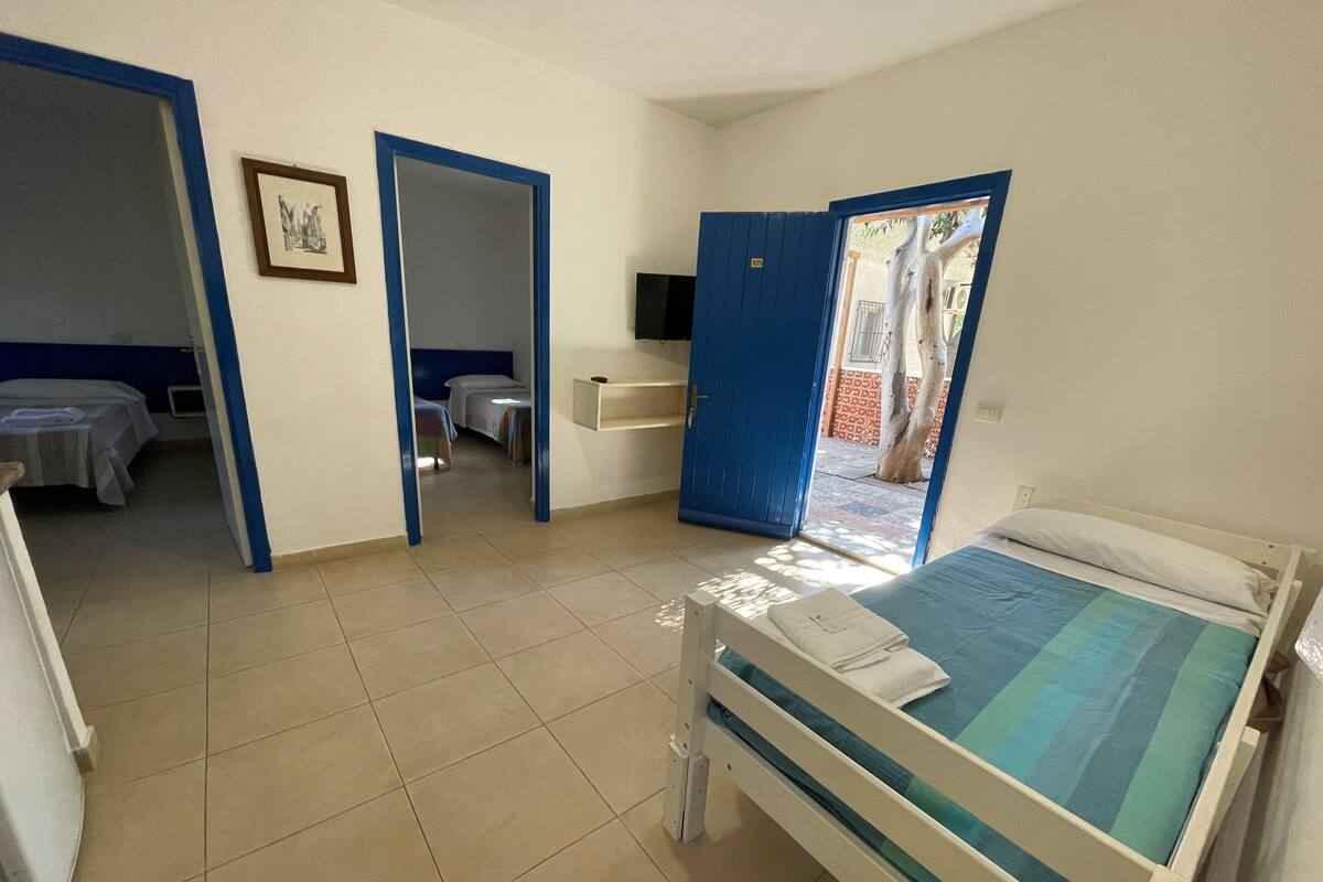 A room with a bed, a desk, and a chair. There is a door leading to another room.