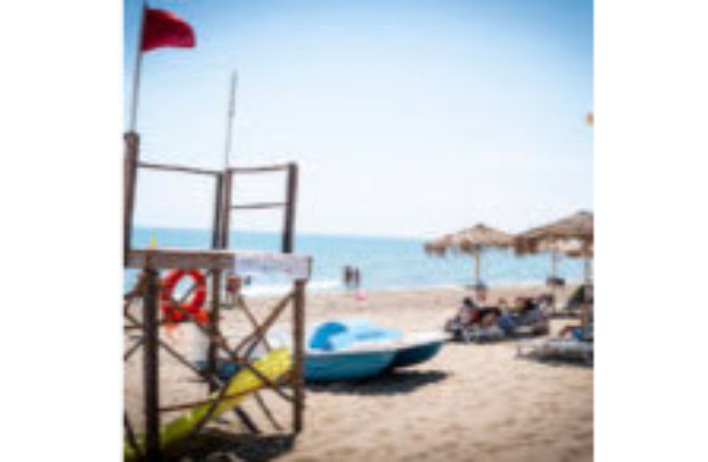 A beach scene with a lifeguard chair, a blue boat, and a thatched umbrella.