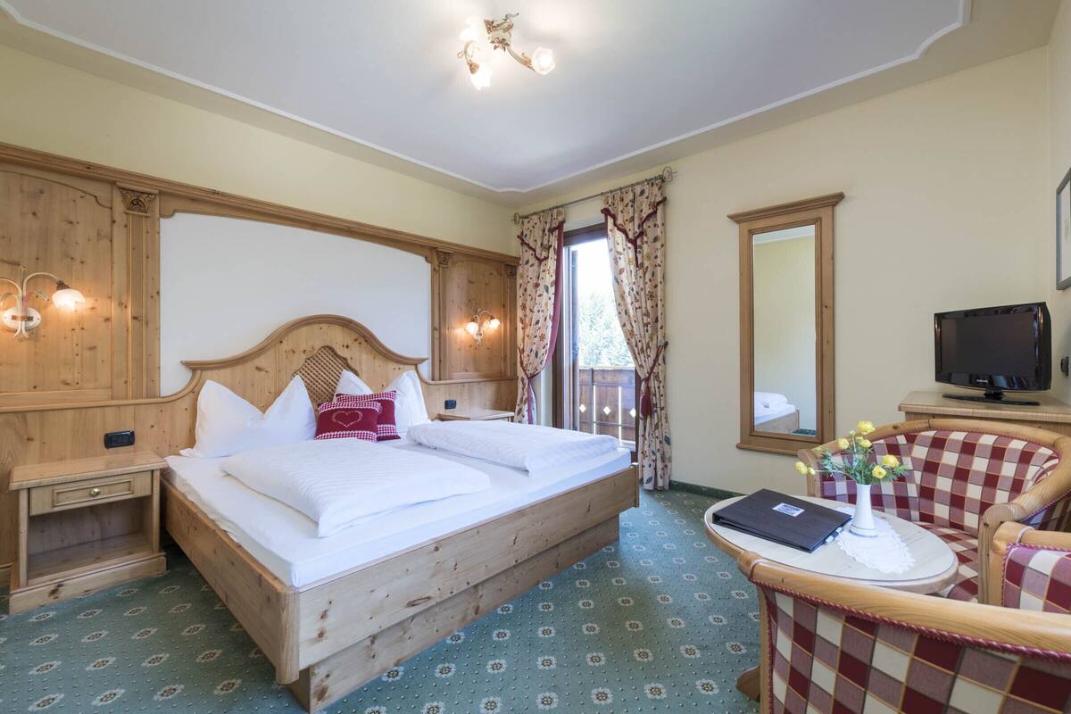 A hotel room with a wooden bed, a desk with a computer, a chair, and a large mirror.