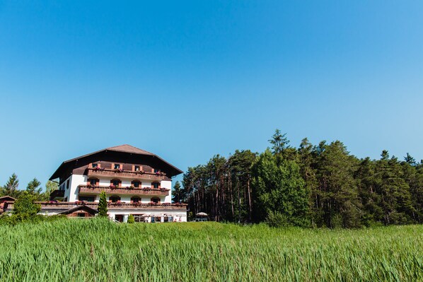A multi-story building with balconies, surrounded by a grassy field and a forest.