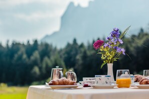 A breakfast table set outdoors with croissants, a vase of flowers, and a glass of orange juice.