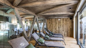 A row of lounge chairs with cushions, wooden beams on the ceiling, and a glass wall with a view of outdoor seating.
