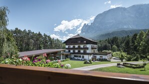 A two-story building with a sloped roof, surrounded by a well-maintained garden and a mountainous backdrop.