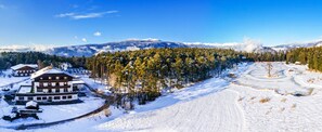 A snow-covered landscape with a lodge, a forest, and mountains in the background.