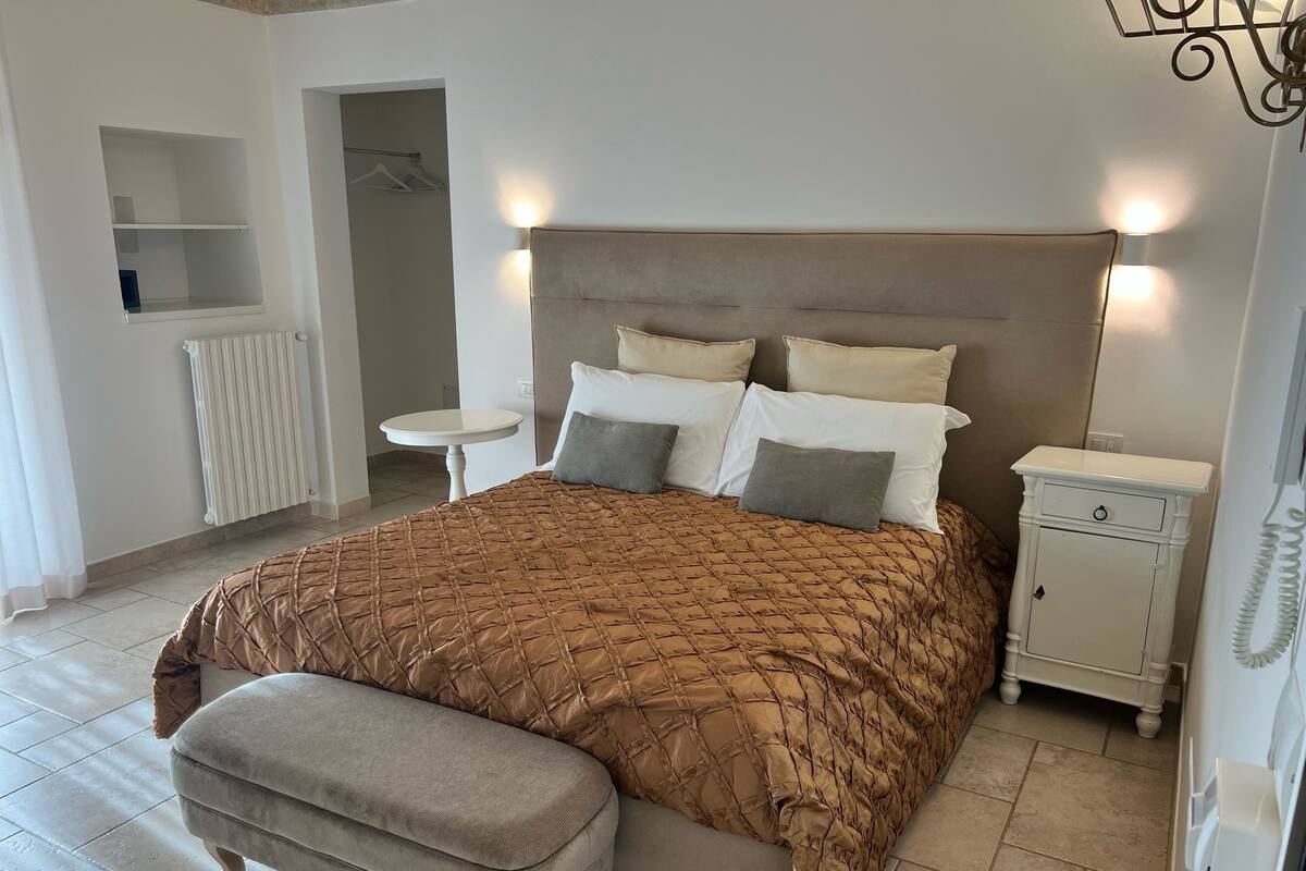 Une chambre bien rangée, avec un grand lit, des tables de chevet, une petite table et un banc.