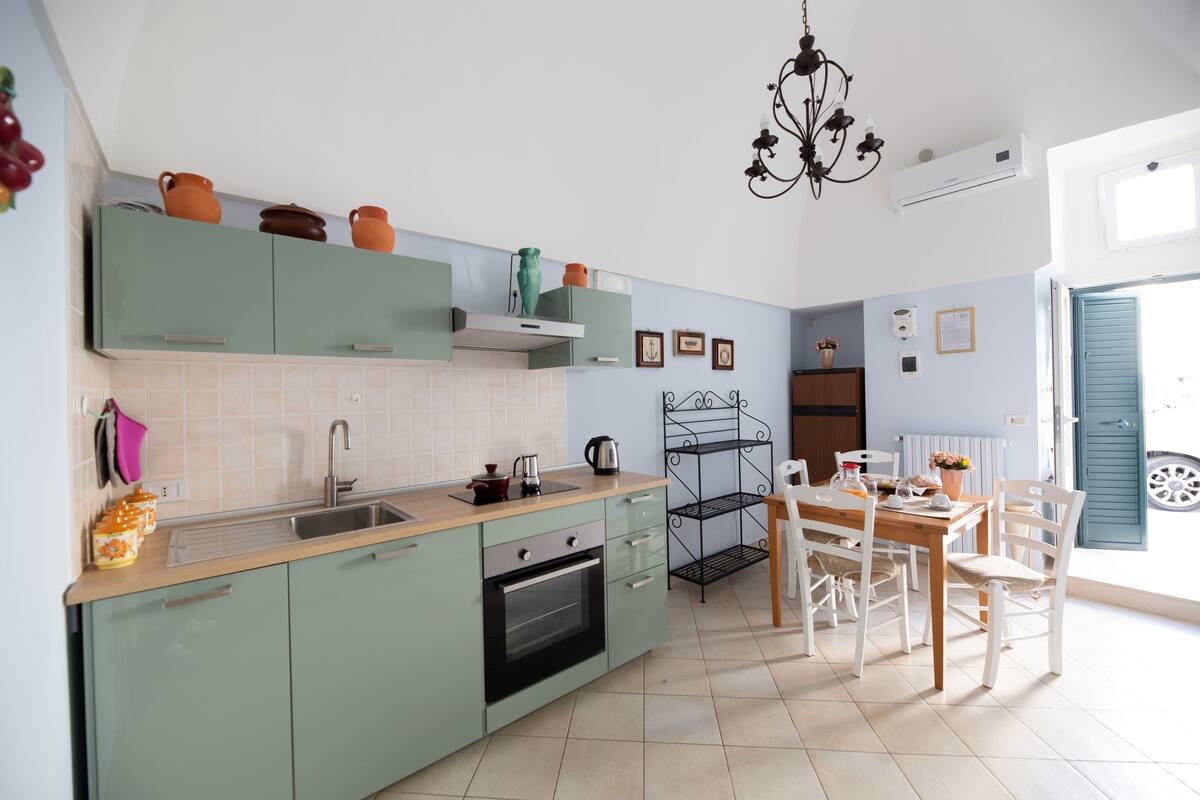 Une cuisine avec des meubles de rangement verts, un évier, une cuisinière et un coin repas comprenant une table et des chaises.