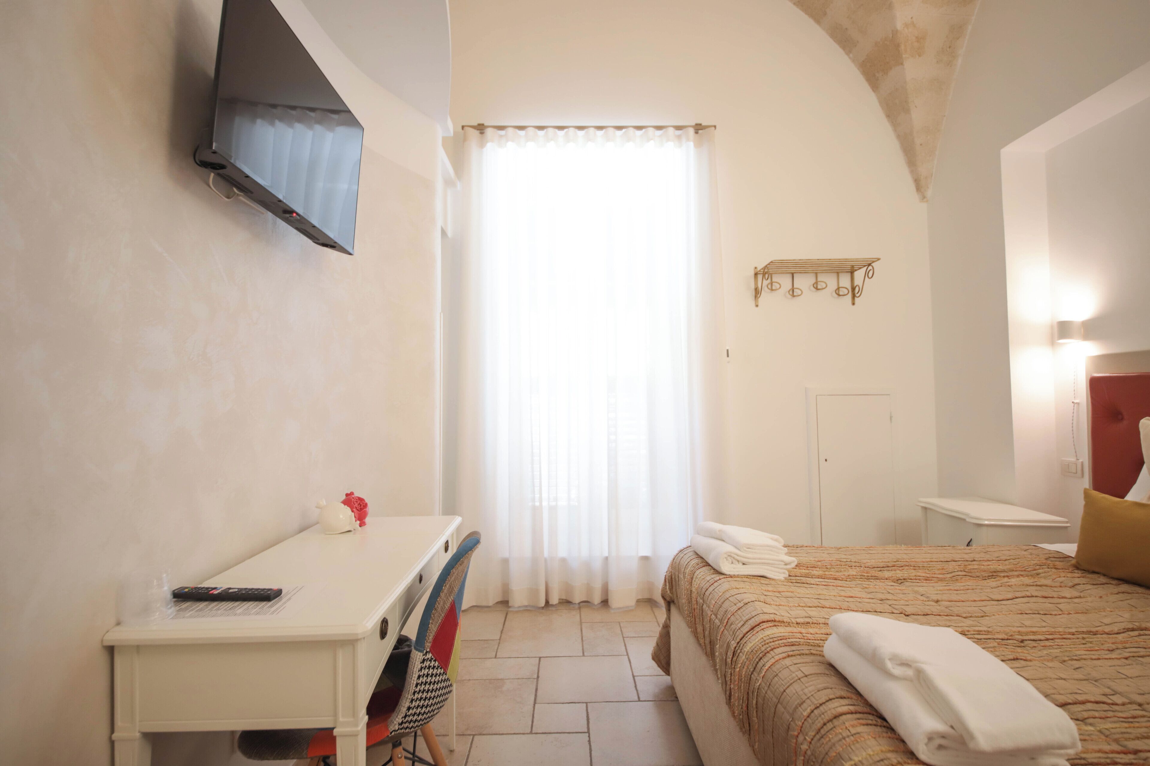 Habitación de hotel con cama, escritorio, silla, televisor montado en la pared y ventana con cortinas.