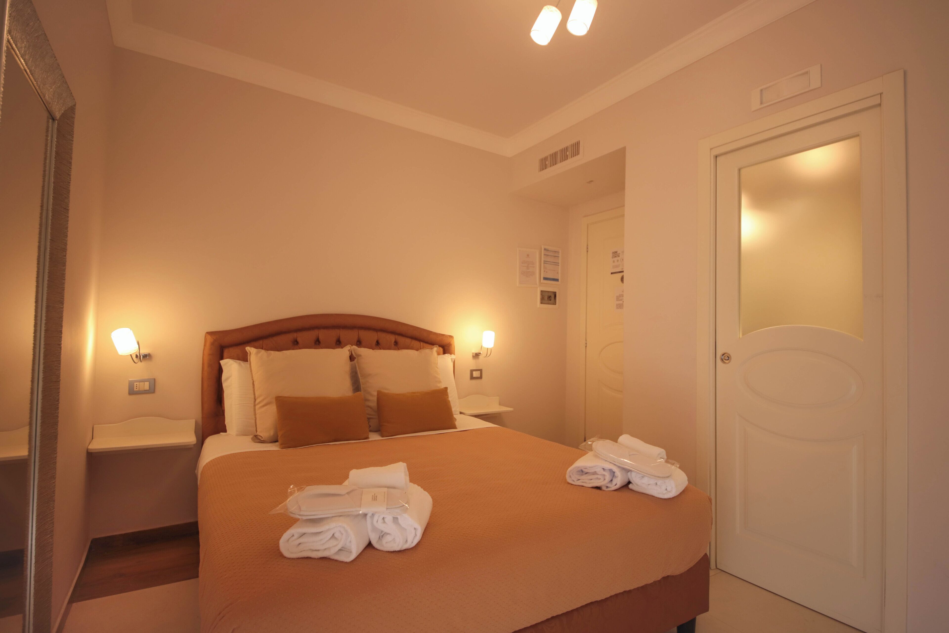 Una camera d'albergo con un letto grande, due comodini, un tavolino e uno specchio.