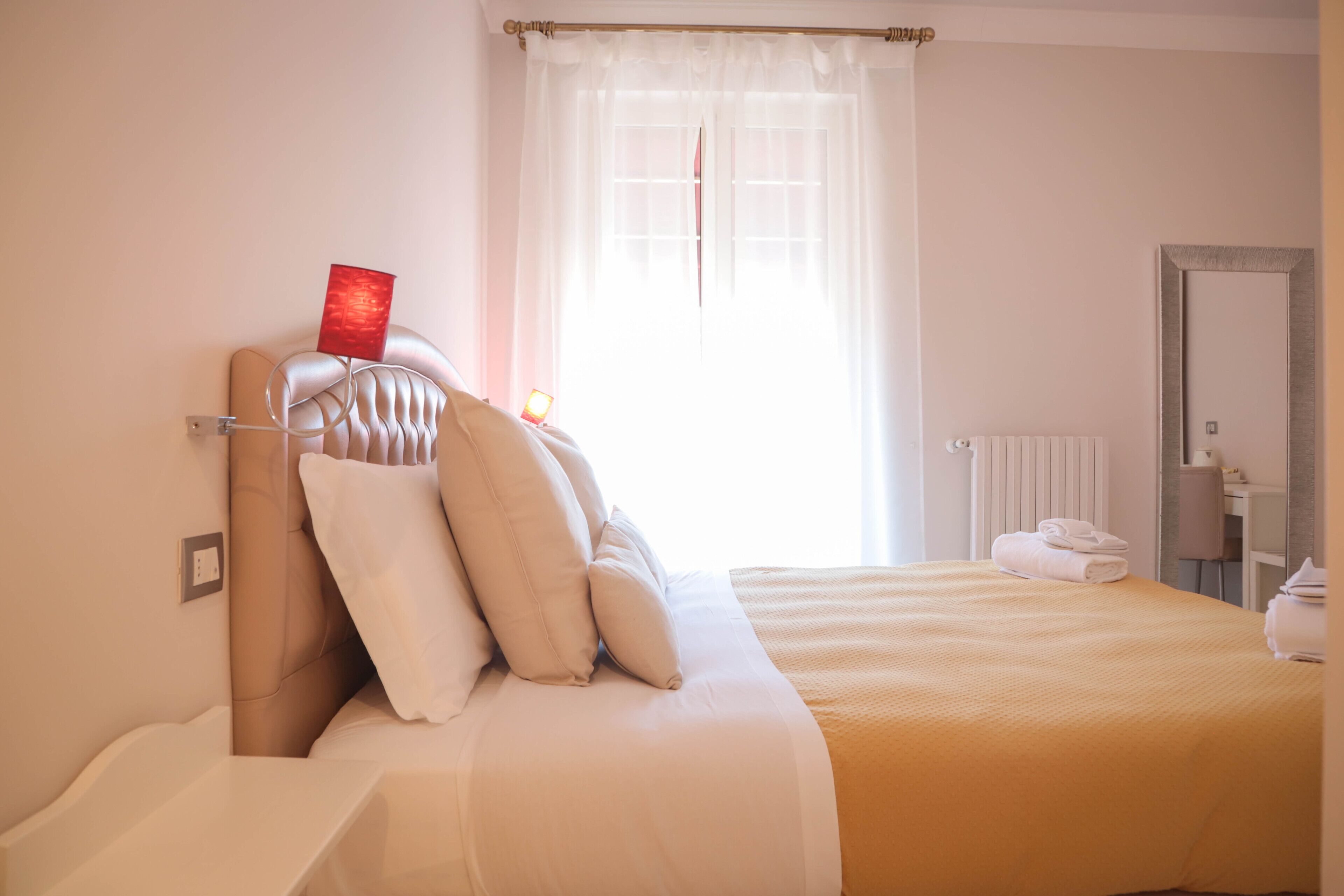 Una cama bien hecha con cabecera, mesita de noche y ventana con cortinas.