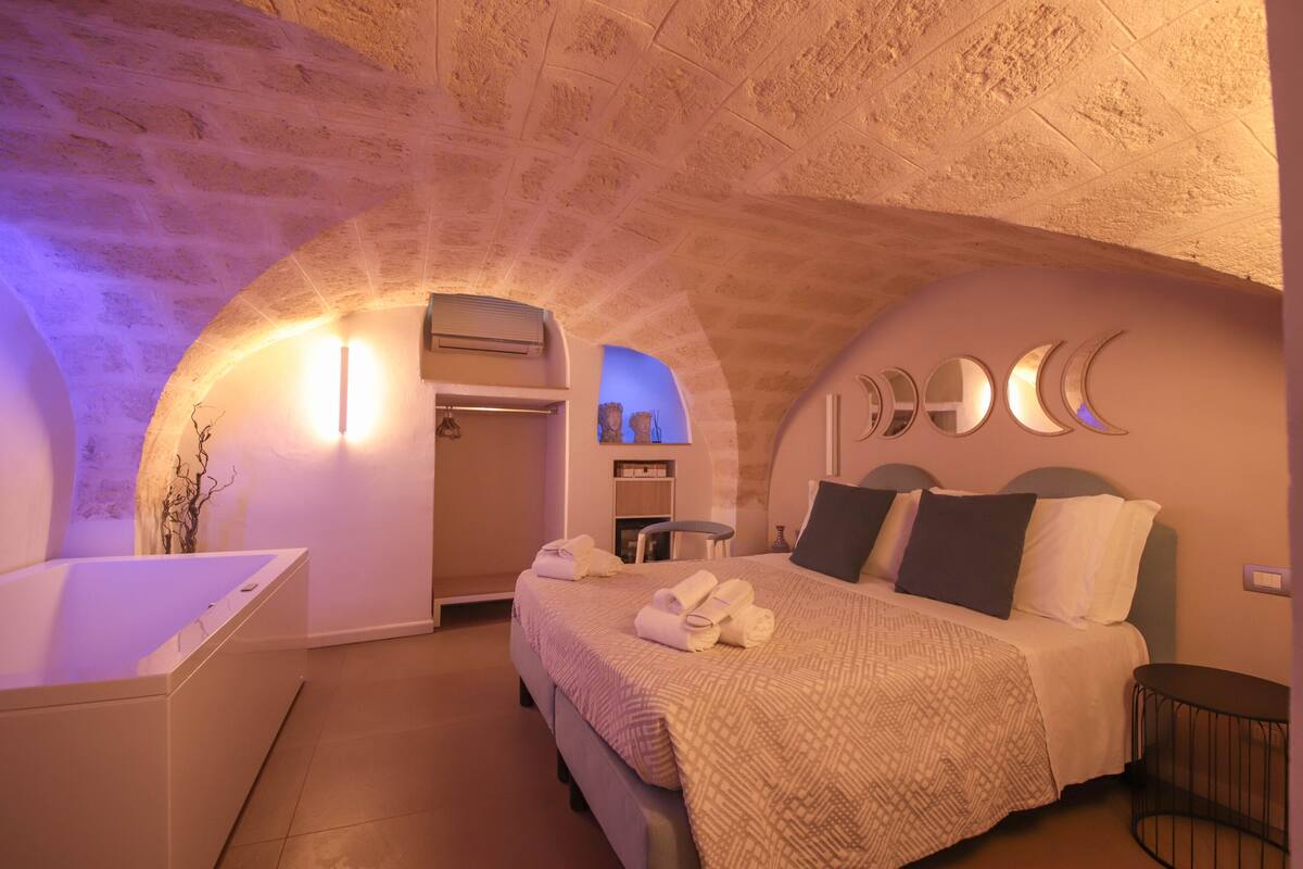 Une chambre à coucher comprenant un lit, une table de chevet, une petite table ronde et une baignoire intégrée.