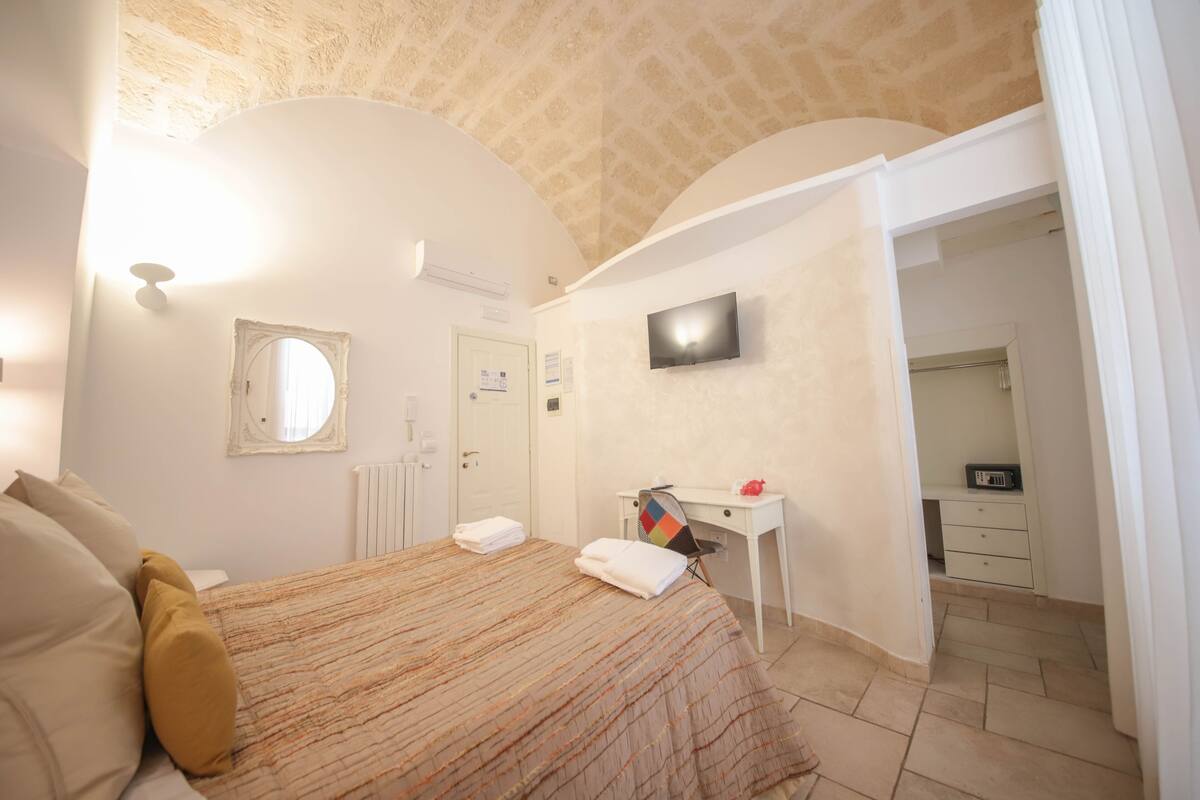 Une chambre d’hôtel avec un lit, un bureau, une télévision et une salle de bain, le tout visible à travers une porte ouverte.