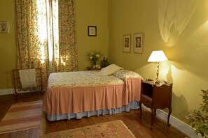 A bedroom with a bed, a nightstand, a lamp, and a window with floral curtains.