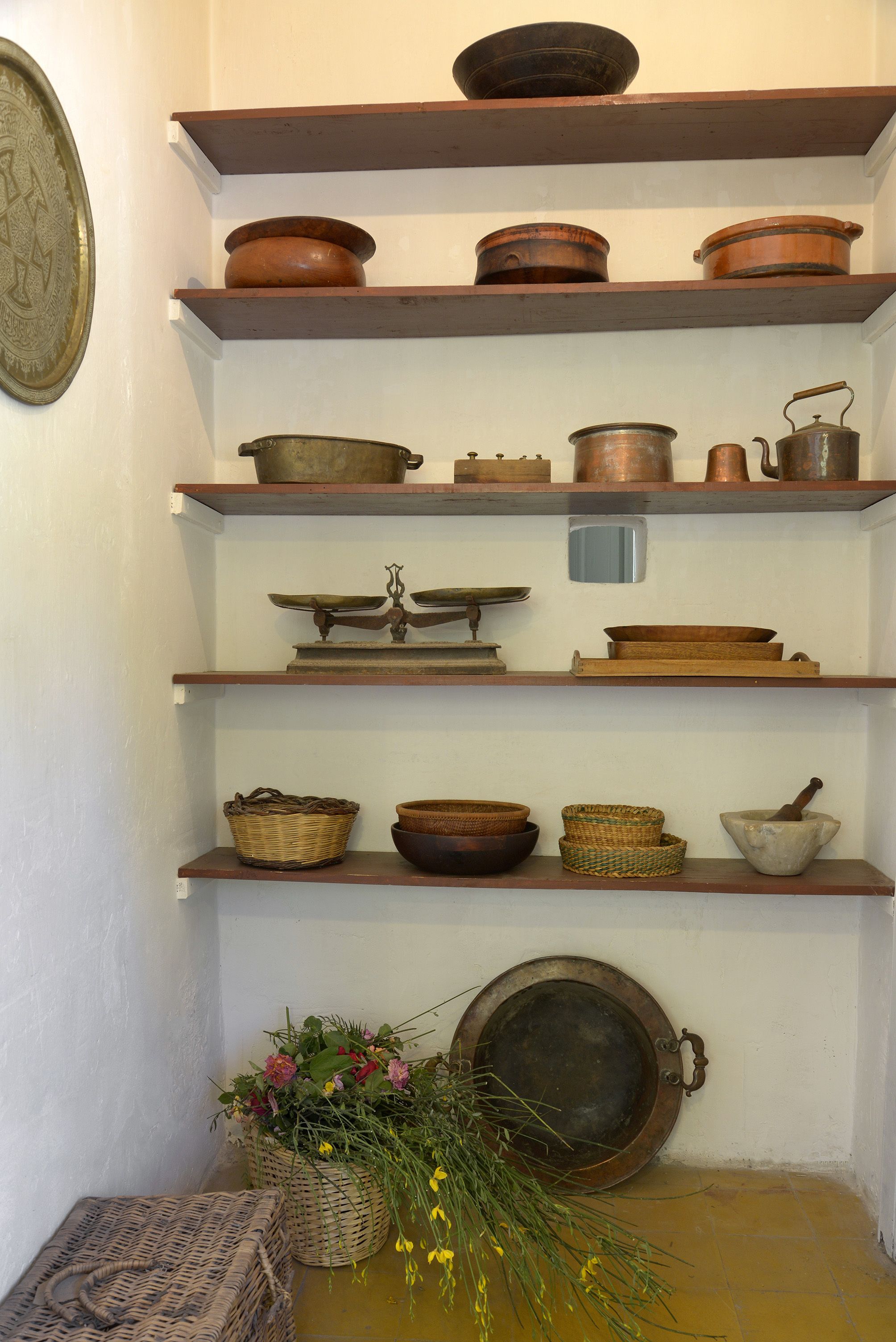 Una exhibición de utensilios de cocina antiguos en estantes, incluyendo ollas, sartenes, una balanza y cestas.
